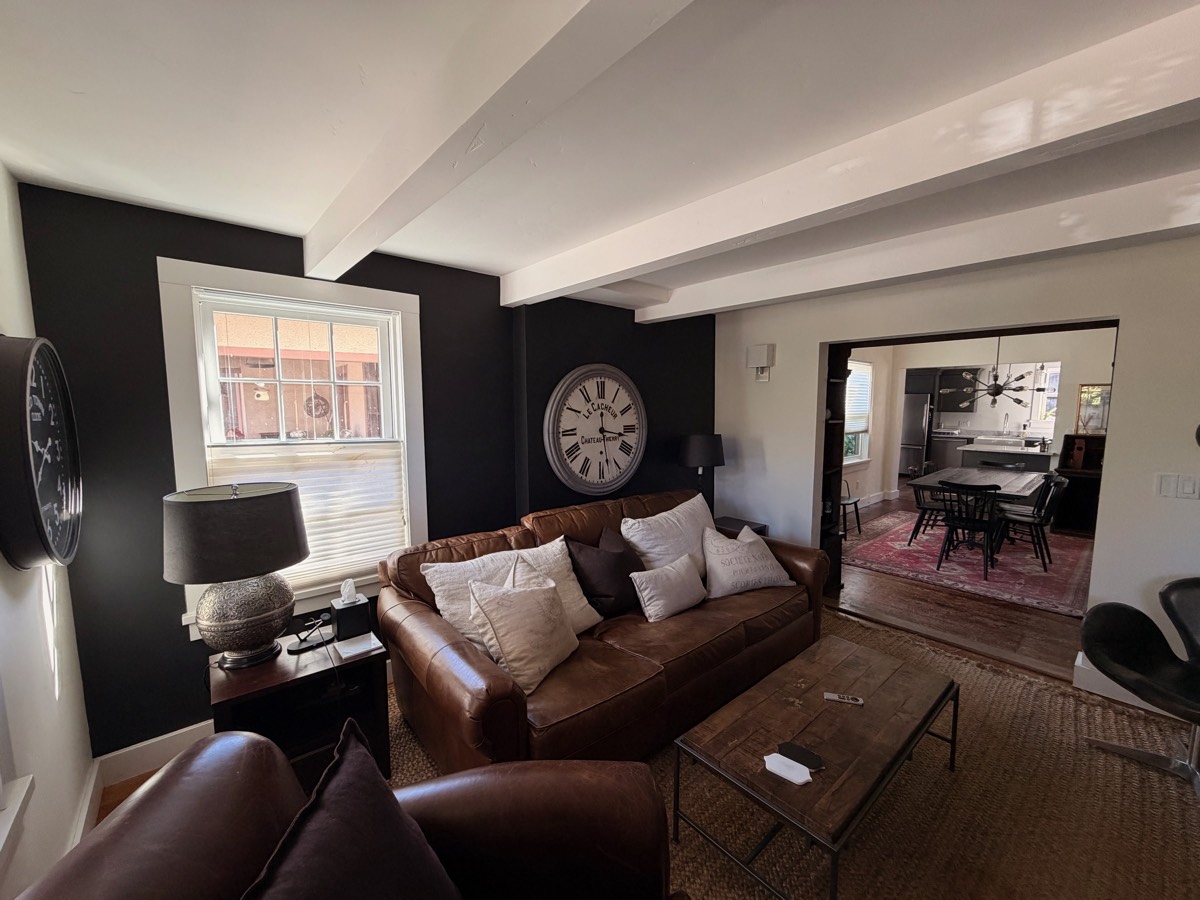 Living room with a brown leather sofa, oversized wall clock and exposed ceiling beams