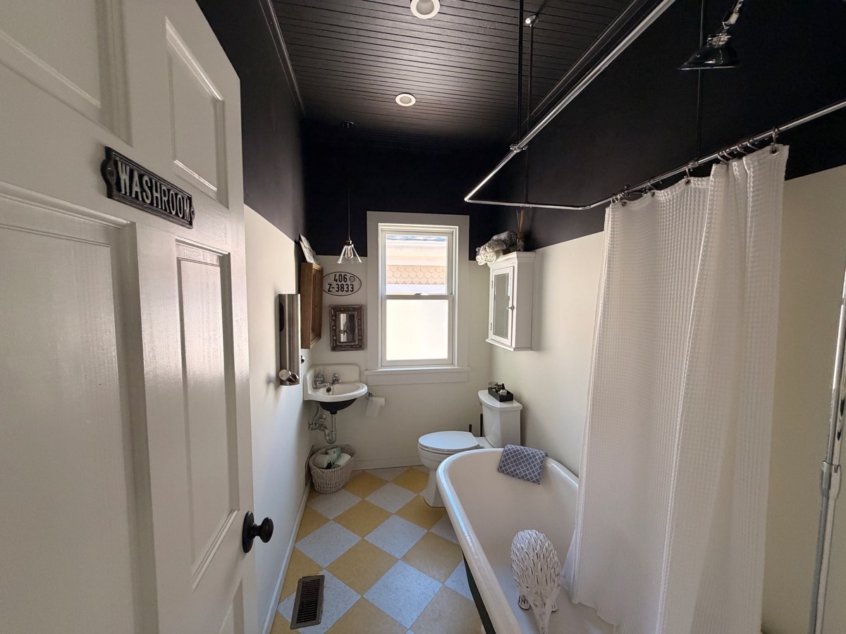 Main-floor washroom with a clawfoot tub and shower, checkered floor and black beadboard ceiling
