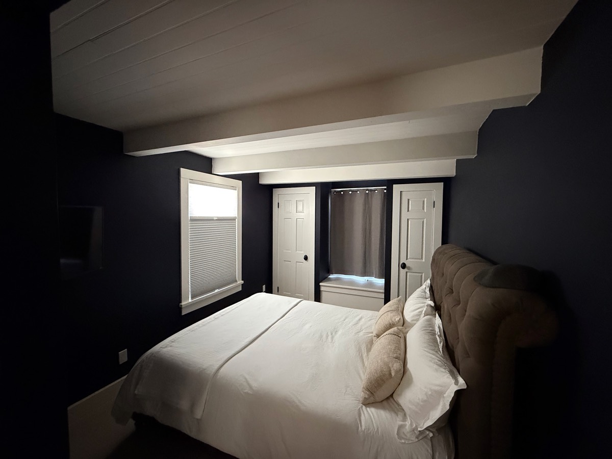 Main-floor bedroom with deep blue walls, white bedding and a tufted headboard