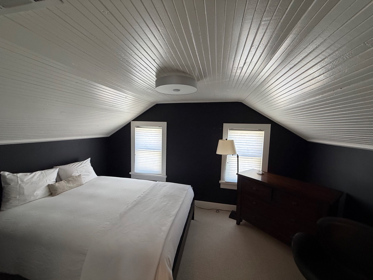 Upstairs bedroom under a vaulted white beadboard ceiling with two windows and a wood dresser
